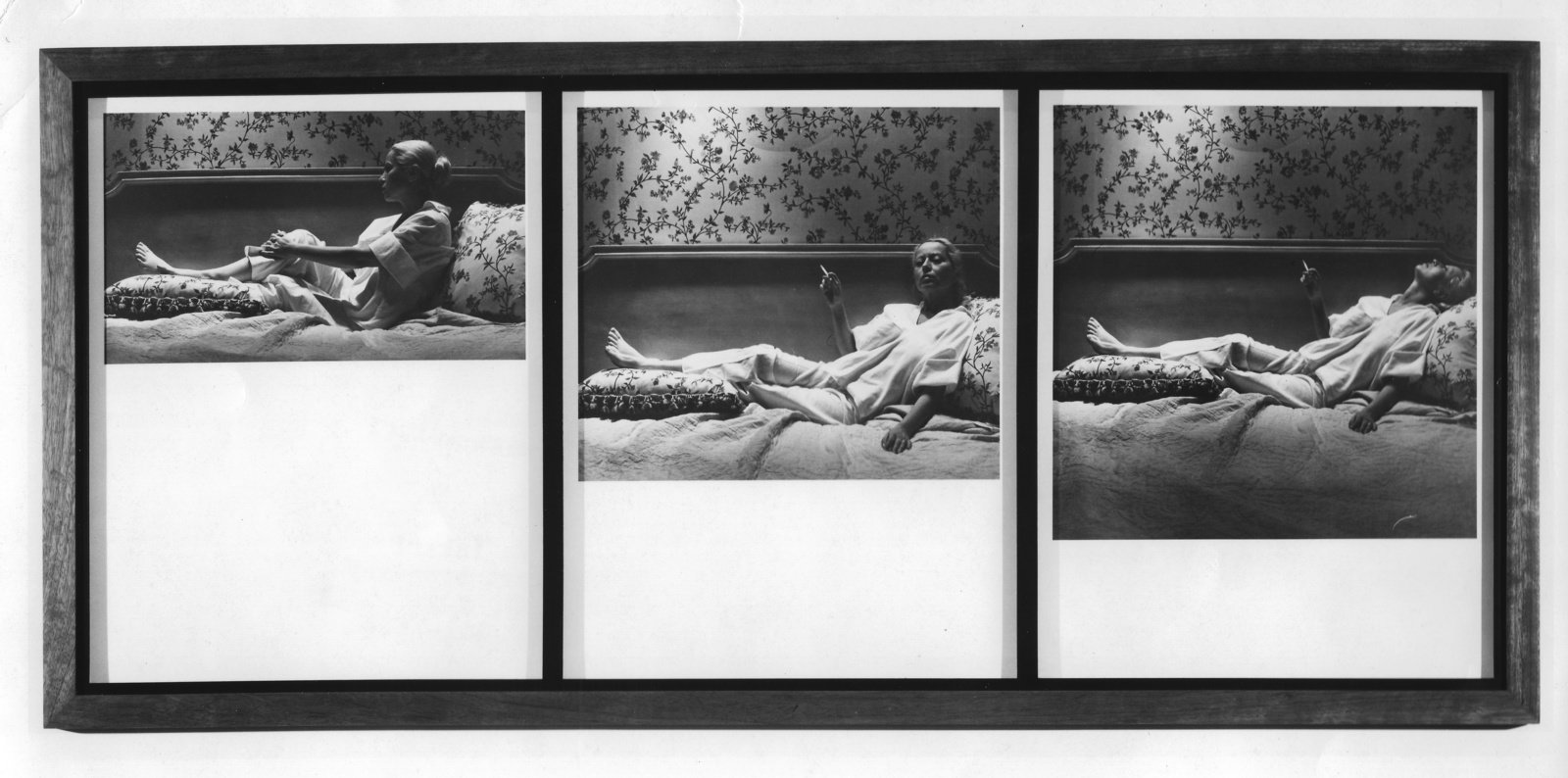 Three framed, black and white, slver gelatin prints by Robert Mapplethorpe of Holly Soloman reclining on a bed while smoking a cigarette. A floral wallpaper pattern that matches the pillows adorns the wall above her. 
