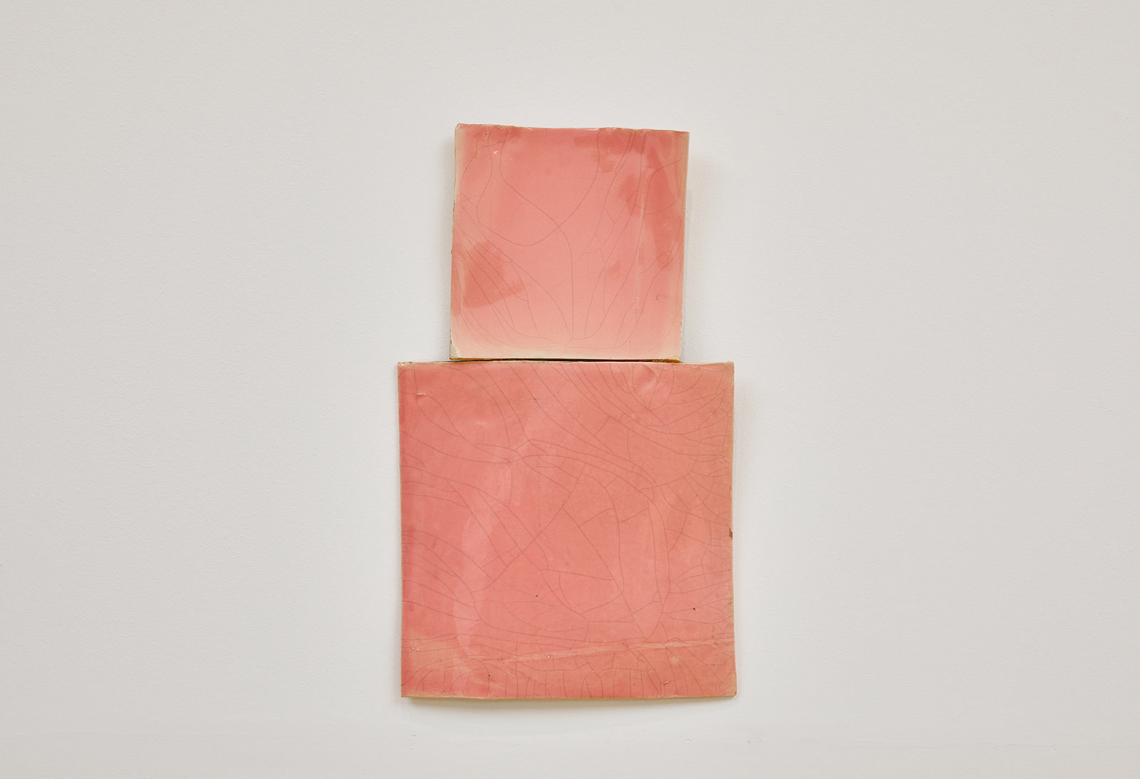 A smaller glazed, pink porcelain square is hung directly above a slightly larger glazed, pink porcelain square by Mary Heilmann.
