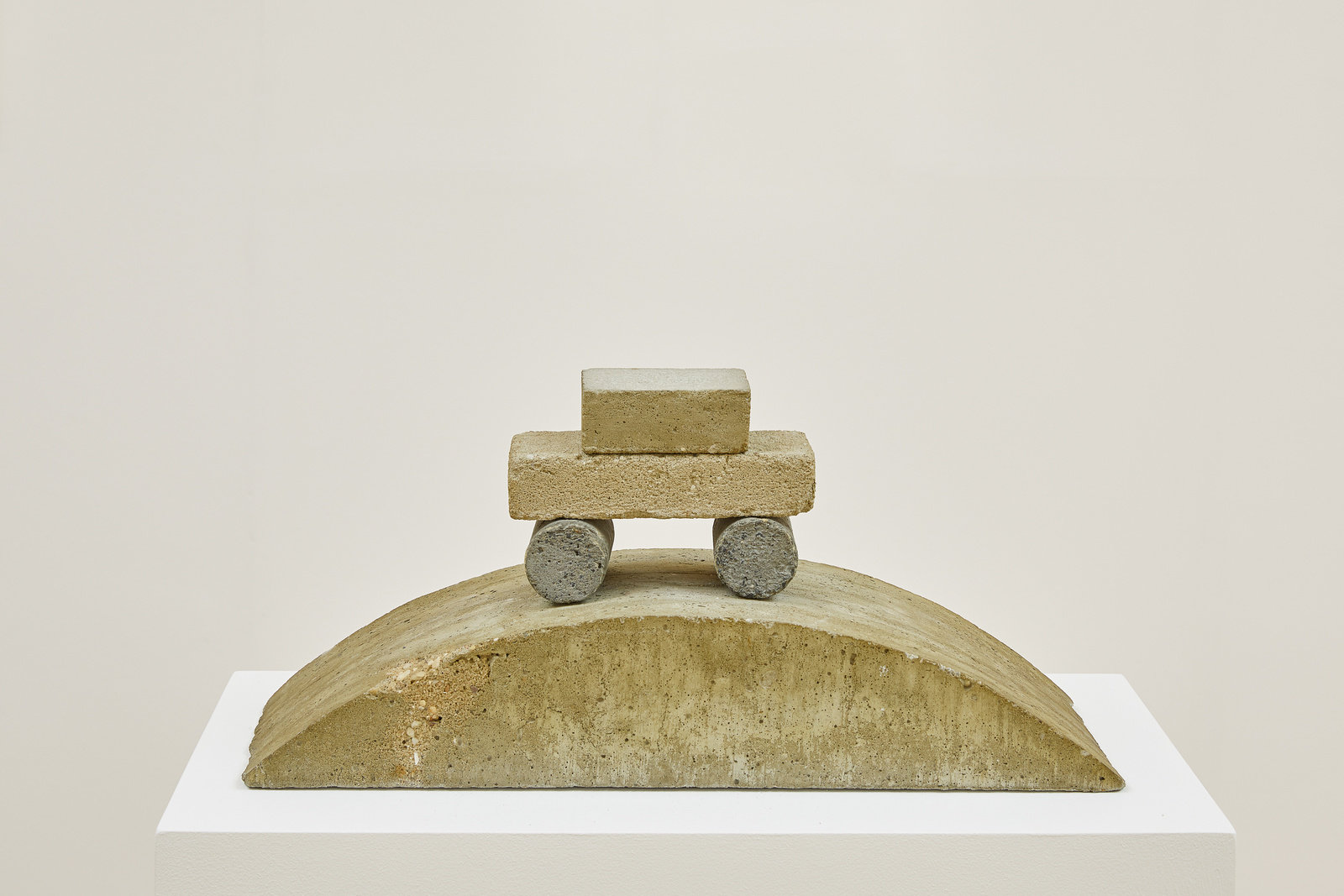 A concrete sculpture by Ned Smyth of an abstracted car sitting on top of a semi-circular base. 