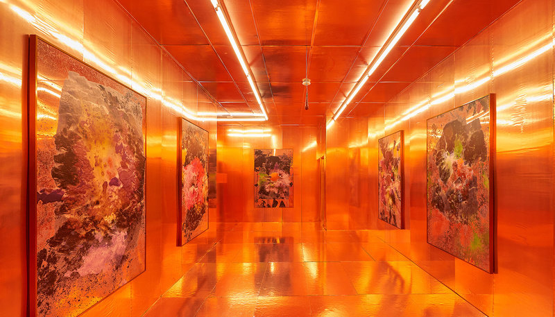 A room covered in orange metallic thermal sheets, with fluorescent lighting and mirrored paintings