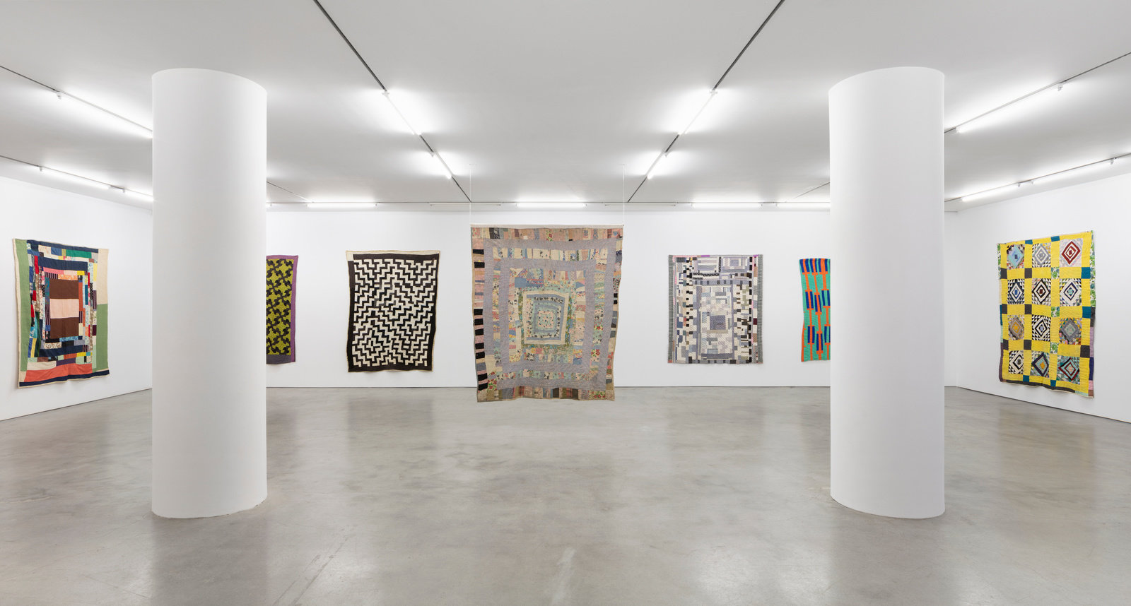An installation view of various quilts displayed on three walls.