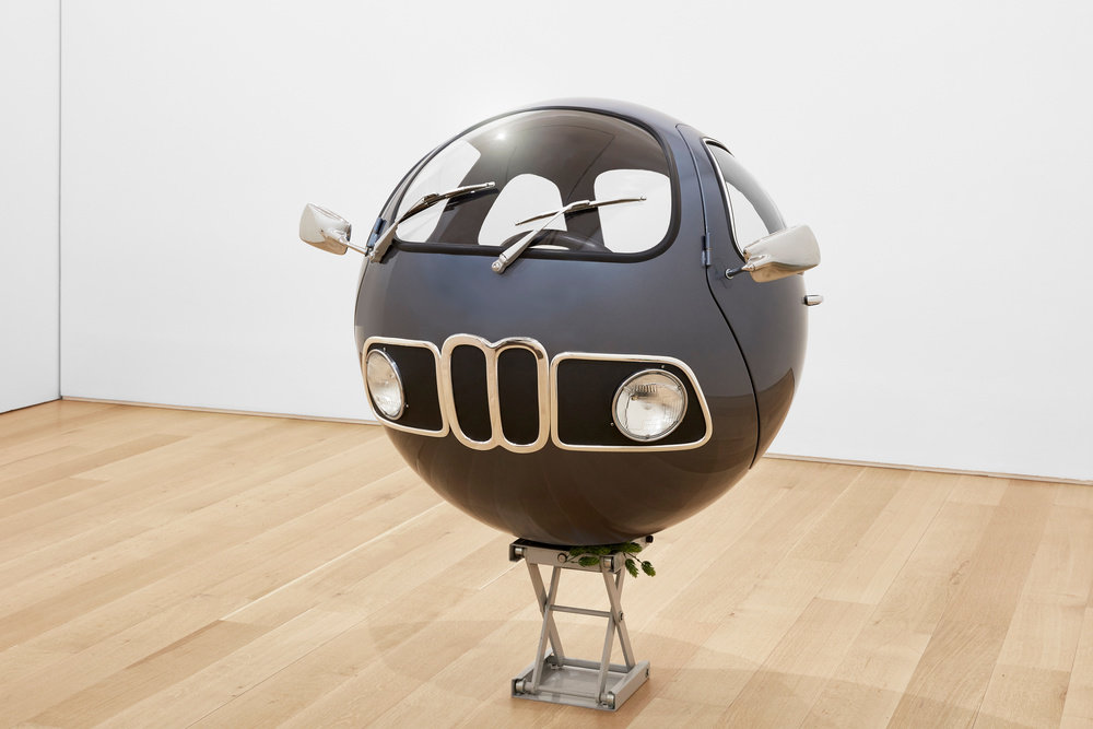A spherical sculpture made of auto parts that sits on a lift jack by Lars Fisk. 