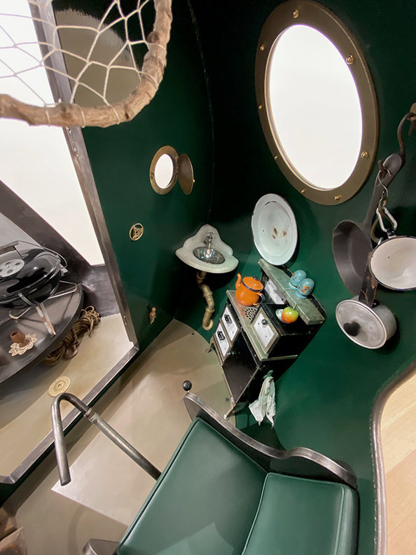 An interior view of the sculpture "Houseboatball" by Lars Fisk. The surfaces are dark green and it is filled with domestic objects. 