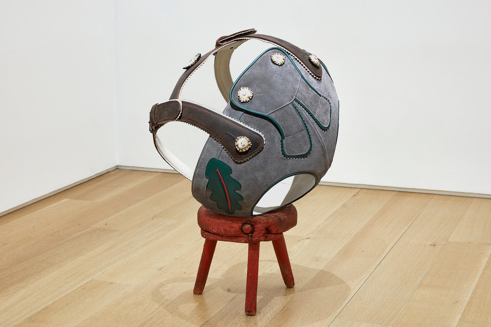 A spherical sculpture that resembles Lederhosen that sits on a red stool by Lars Fisk. 