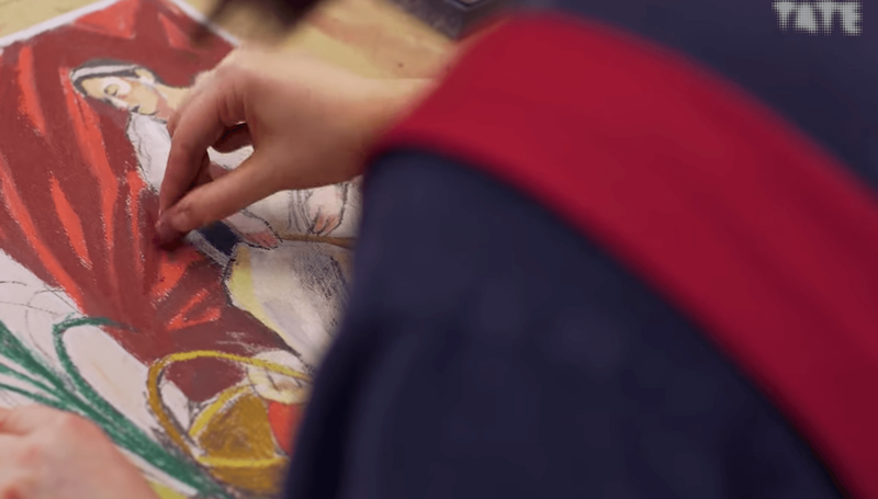 An artist's hand working on a pastel drawing, viewed from over the left shoulder